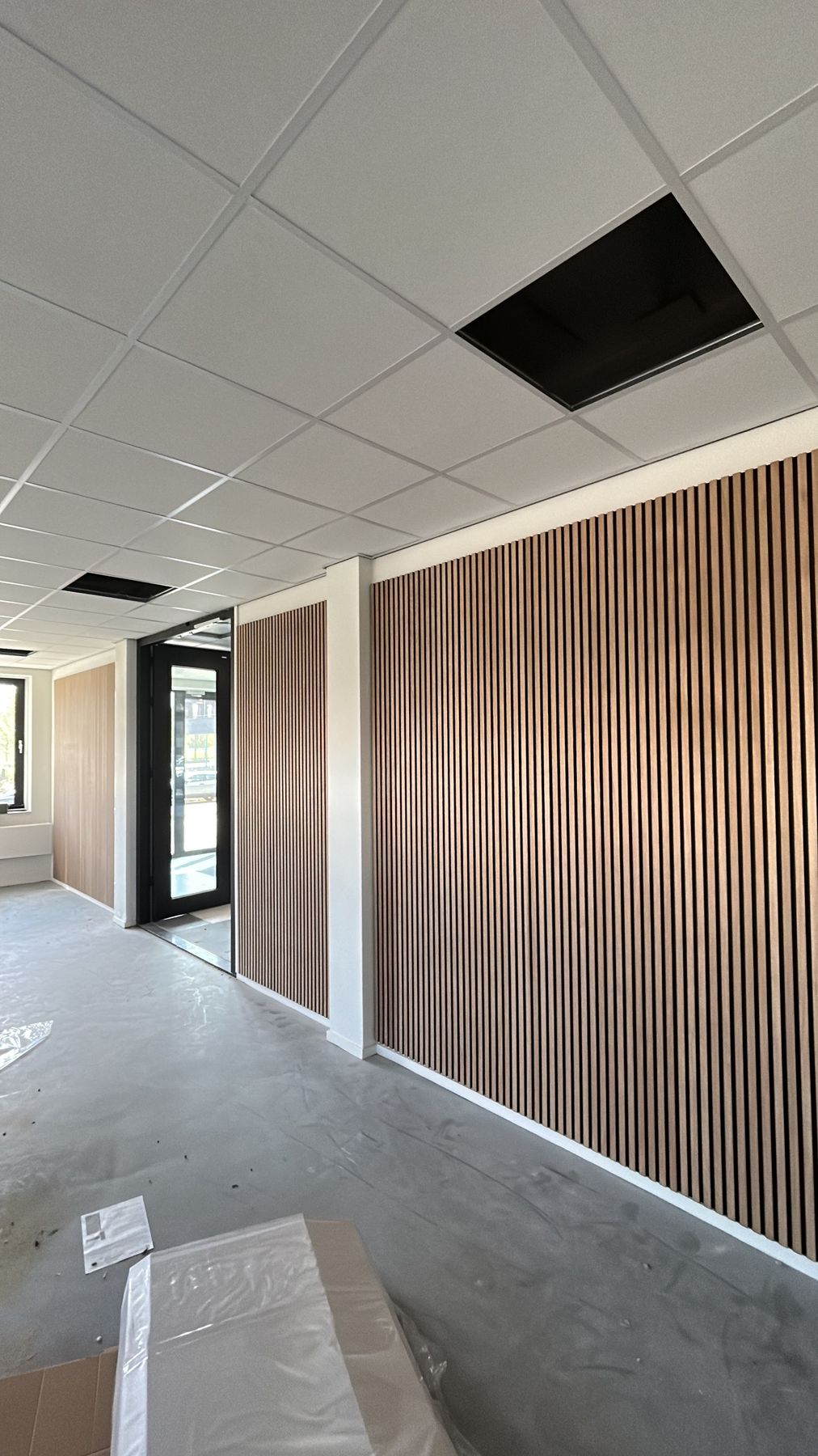 Afgewerkte ruimte met een donkere houten lamellenwand, glazen deuren en systeemplafond