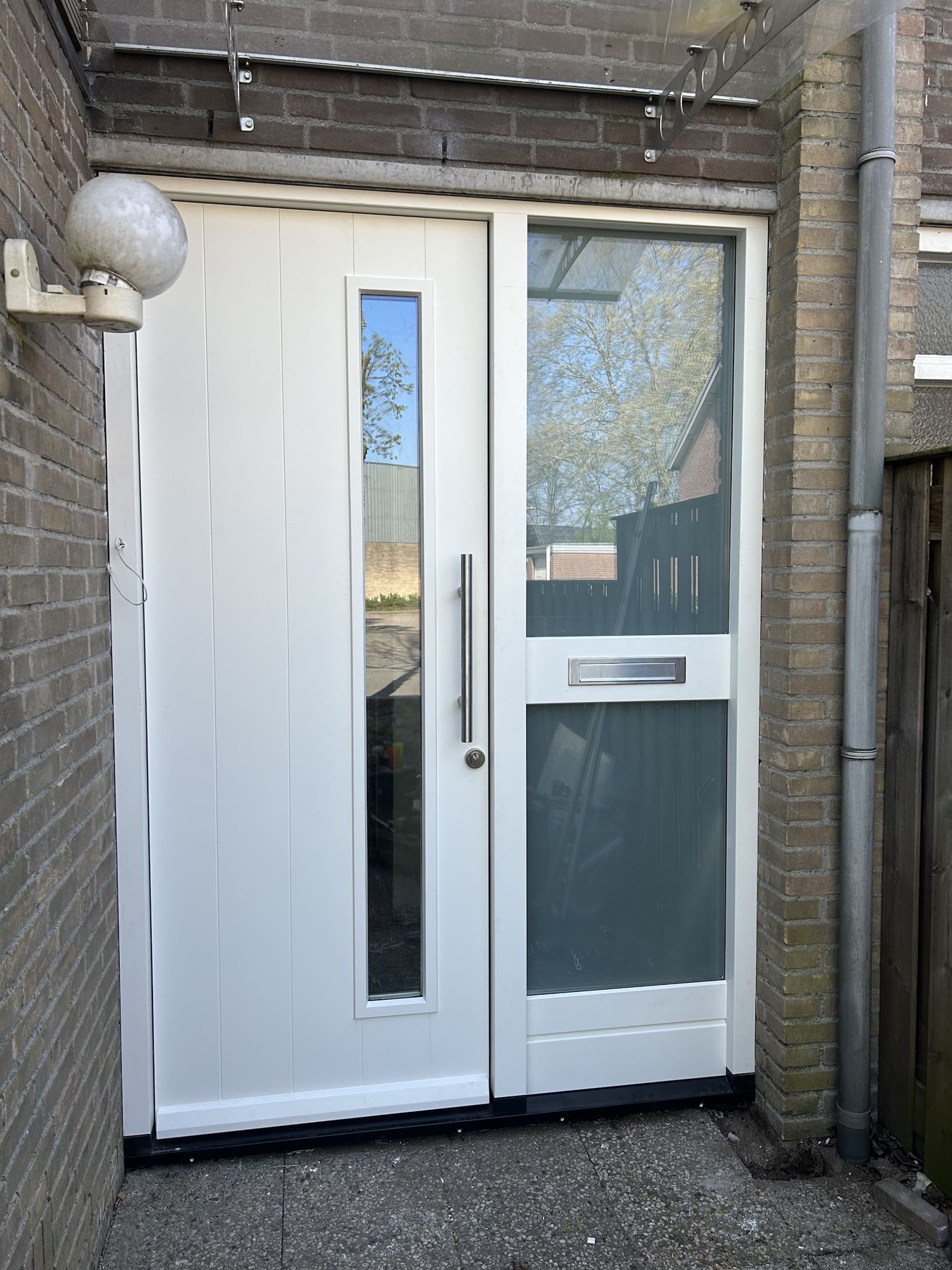 Nieuwe witte voordeur met glazen zijlicht in een bakstenen portiek