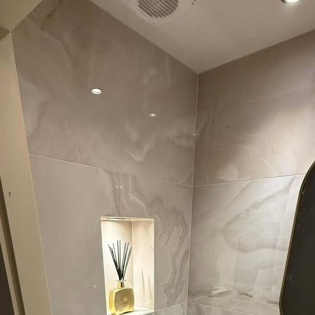 Gerenoveerd toilet met grote marmerlook tegels, verlichte nis en inbouwspots